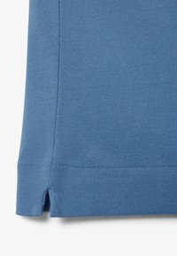 Close-up van de zoom van blauwe gebreide stof met zijsplit en zichtbare stiksel details.