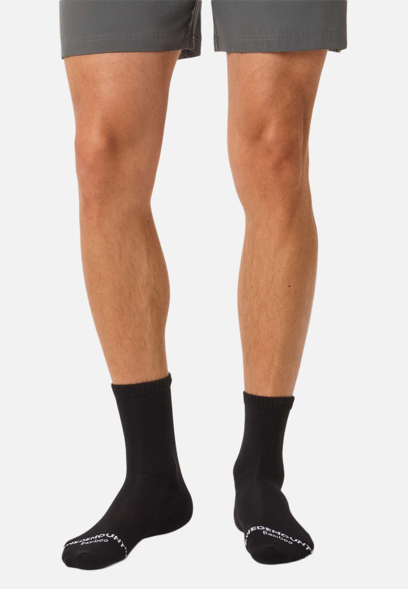 Schwarze Knöchelsocken aus Bambusmaterial mit geripptem Bündchen, glatter Textur und einem weißen Logo am Fußgewölbe.