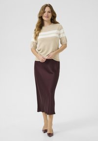 Suéter de punto beige con rayas blancas, combinado con una falda midi de satén burdeos oscuro. Modelo lleva tacones puntiagudos burdeos.