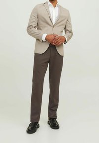 Béžové pruhované sako s jedním knoflíkem, doplněné tmavě šedými kalhotami. Celý outfit doplňují černé lesklé boty. Hladká látka a strukturovaný střih.