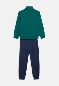 Πράσινο, μακρυμάνικο πουλόβερ με γιακά mock neck και σκούρο μπλε φόρμες. Μείγμα βαμβακιού, απαλή υφή, μανσέτες και μέση με ριμπ ύφανση.