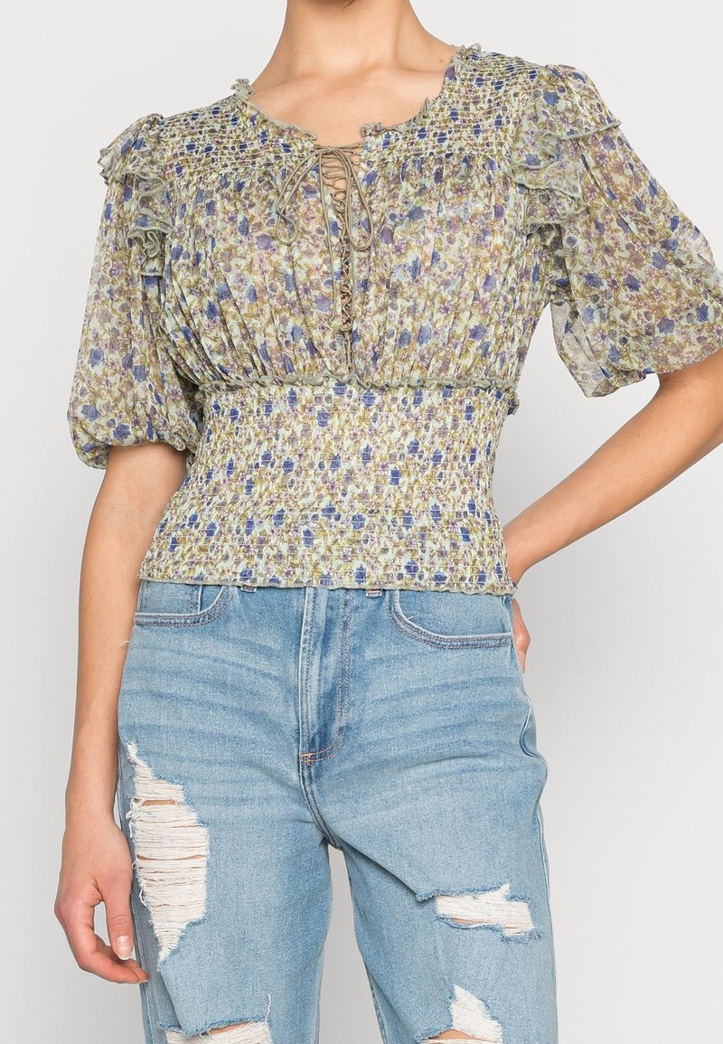 Blus med puffärmar och blommönster, med smockad midja, snörning i halsringningen och strukturerad, lättvikts tyg i gröna och lila nyanser.