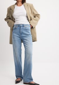 Ljusblå jeans med hög midja, rak benstil och blekt utseende, i kombination med en beige oversized blazer och svarta spetsiga ballerinas.
