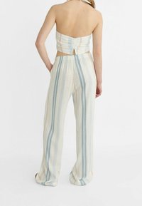 Zweilagiges Outfit mit einem geraden Cropped-Top mit einem Schlüssel-ausschnitt am Rücken und lockeren, gestreiften Hosen in sanften Farben wie Blau, Beige und Pink.