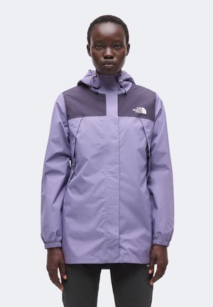 Osoba nosiaca dvojfarebnú fialovú bundu North Face s kapucňou, predným zipsom a logom na hrudi, stojaca pred jednofarebným pozadím.