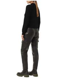Schwarzer Strickpullover, figurbetont; kombiniert mit schwarzen Leder-Cargo-Hosen mit Seitentaschen. Fußbekleidung: schwarze Stiefeletten mit grünen Sohlen.