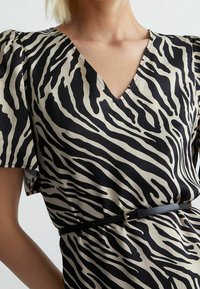 Robe imprimée animalière avec un décolleté en V, des manches courtes bouffantes, et une taille ajustée avec une ceinture noire. Le tissu a une texture lisse.