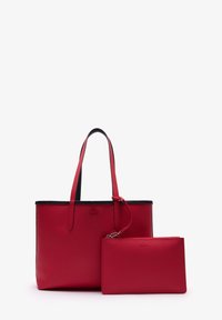 Bolso tote de cuero rojo con textura de grano y acentos en negro, con dos correas largas, acompañado de un monedero a juego con cremallera. Ambos artículos tienen textura.