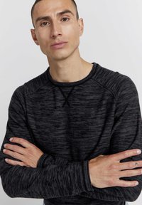 Schwarzes Langarmshirt mit strukturiertem Muster, Rundhalsausschnitt und Raglanärmeln. Weicher Stoff; lockere Passform mit detailliertem Ausschnitt.