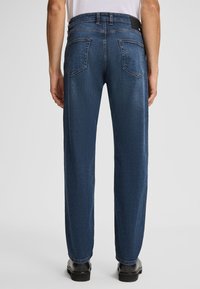 Jeans denim w ciemnoniebieskim kolorze z prostymi nogawkami, z dwiema tylnymi kieszeniami i czarną skórzaną naszywką na pasku.