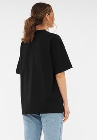 Czarna, oversize koszulka z bawełny, z krótkimi rękawami, okrągłym dekoltem i prostym wykończeniem, noszona z jasnoniebieskimi dżinsami.