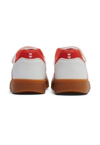 Weiße Sneaker mit roten Akzenten. Merkmale sind ein glattes Obermaterial aus Synthetik, ein Klettverschlussriemen und eine Gummisohle mit strukturierten Details.