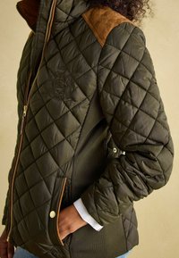 Zelena jakna s ušivom, s smešnim antilop naglascima na ramenima, zatvaranjem na rajsferšlus, bočnim džepovima i rebrastim manžetama. Ima logo na prsima.