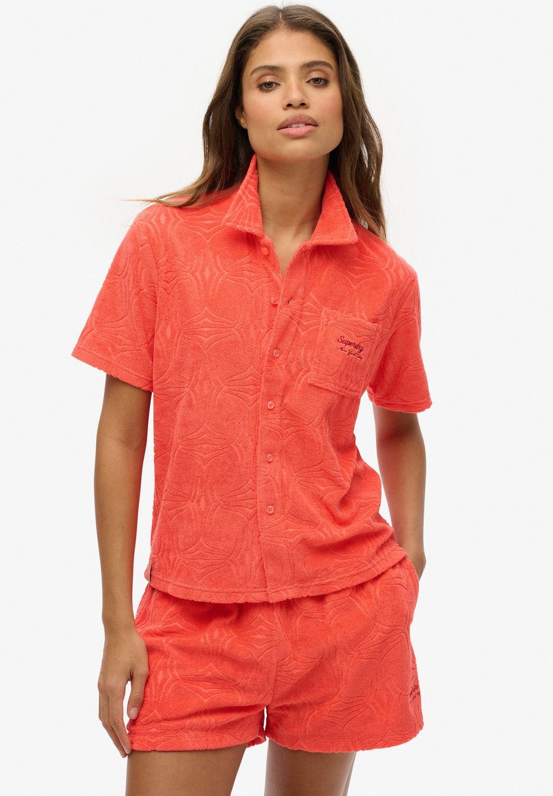 Chemise à manches courtes en éponge corail avec un motif texturé, boutons sur le devant et une poche poitrine avec un logo brodé. Shorts assortis inclus.
