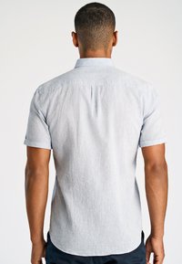 Koszula z krótkim rękawem na guziki w jasnoniebieskim kolorze z delikatną teksturą, z klasycznym kołnierzykiem i detalem w plecach.
