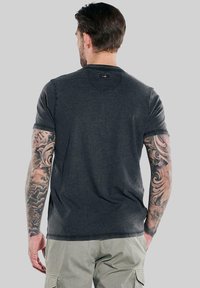Dark gray short-sleeve t-shirt made of soft fabric, featuring a round neckline and raw edges, worn with light green cargo pants.