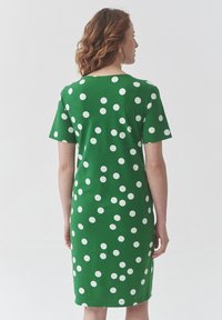 Zelena haljina s kratkim rukavima i do koljena, ukrašena bijelim točkicama, izrađena od glatkog materijala.