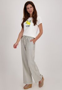 Witte t-shirt met citroen grafiek en "Limone" tekst, gecombineerd met wijde gestreepte broek in beige en marineblauw. Plateau-sandalen.