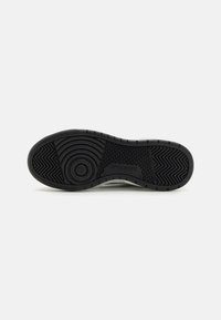 Must musta sneakeripõhi, millel on tekstuurilised mustrid, ringikujulised disainid ja silmapaistev logo. Materjal on painduv ja vastupidav.