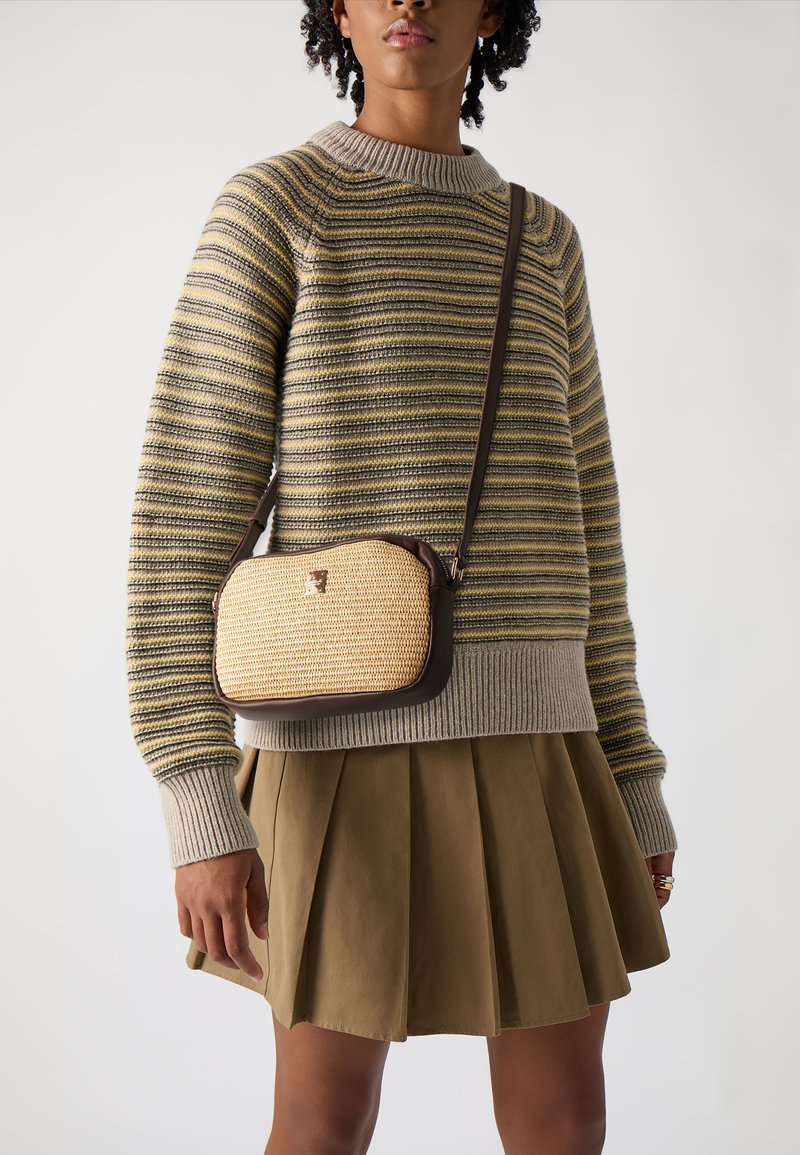 Maglione a righe in tonalità di verde e giallo tenue, abbinato a una gonna plissée color khaki. Piccola borsa a tracolla con texture intrecciata e dettagli marroni.