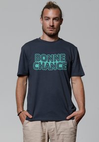 Navy blauwe katoenen t-shirt met turquoise tekst "BONNE CHANCE" in een vet, blokkerig lettertype. Korte mouwen en een relaxte pasvorm.