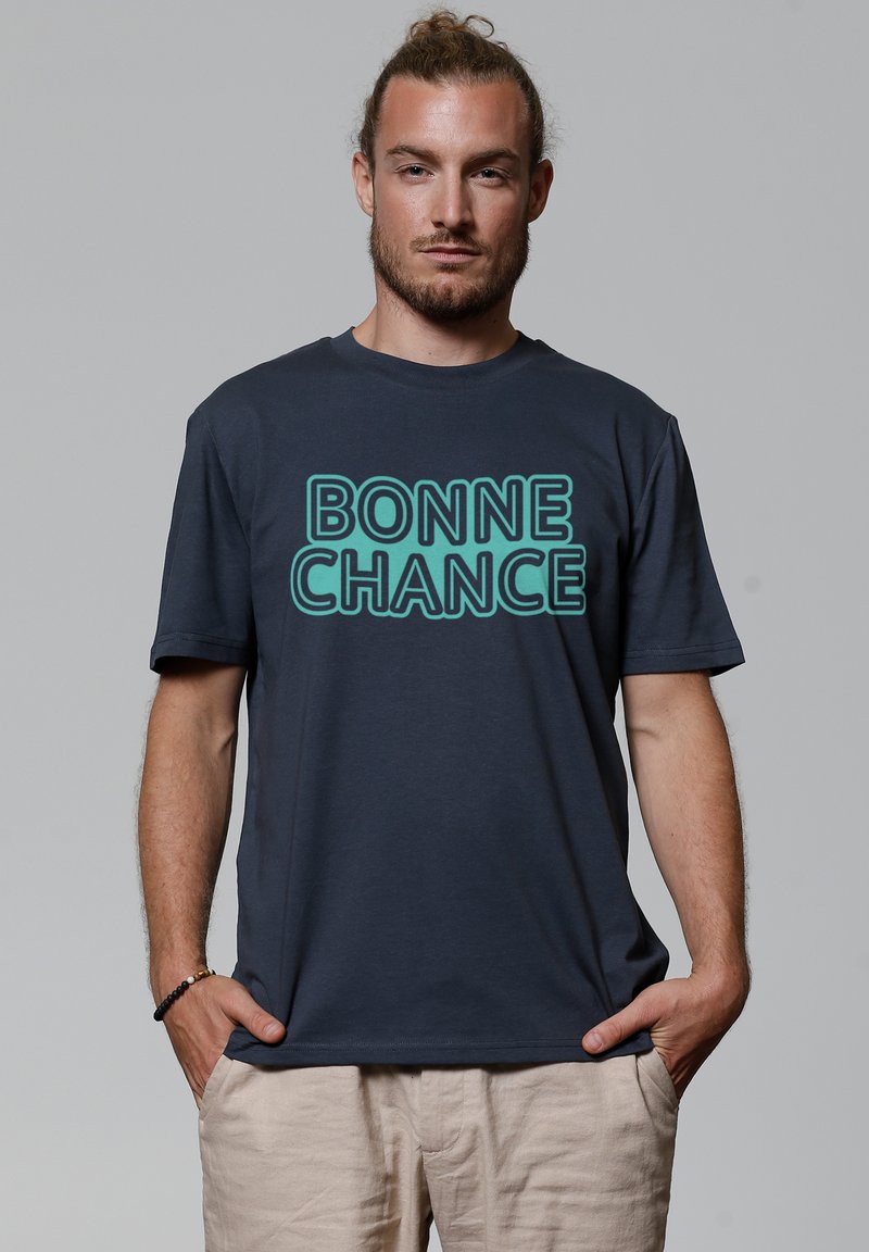 Navy blauwe katoenen t-shirt met turquoise tekst "BONNE CHANCE" in een vet, blokkerig lettertype. Korte mouwen en een relaxte pasvorm.