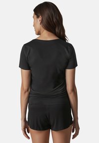 Cămașă sport neagră cu mâneci scurte, textură netedă, croi lejer, combinată cu șorturi negre. Design simplu, detalii minime.