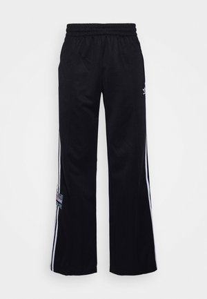 Czarne spodnie dresowe Adidas z białymi trzema paskami po bokach, zestawione z czarną bluzką i białymi trampkami z różowymi akcentami.