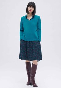 Teal trui met een kraag, gecombineerd met een donker bloemenrok en bordeauxrode laarzen tot de knie. Glad textuur, comfortabele pasvorm en gelaagd ontwerp.