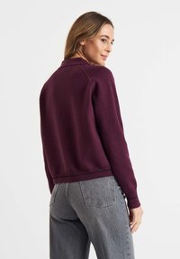 Bordeaux gebreide trui met een kraag en een geribbelde zoom, gecombineerd met grijze hoge taille jeans met achterzakken en een gladde textuur.