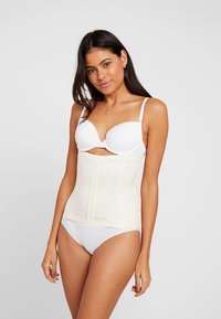 Gestionnaire de taille beige avec motif floral transparent, fermeture avant réglable et texture lisse, porté sur un soutien-gorge et des sous-vêtements blancs.