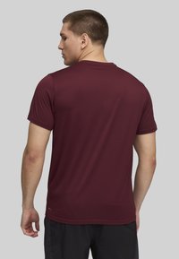 Camiseta deportiva color marrón con mangas cortas, cuello redondo y una textura suave. Presenta un logotipo discreto en el dobladillo inferior y un ajuste relajado.