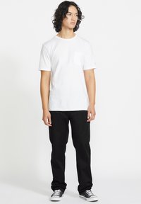 White short-sleeve t-shirt with a pocket, paired with black trousers and black sneakers. Smooth texture, simple design, casual fit.