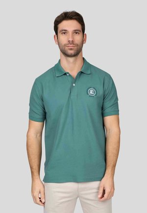 Polo vert avec col, manches courtes et un petit emblème sur la poitrine gauche. Fabriqué en coton lisse, design ajusté.
