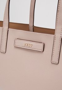 Sac à main en cuir texturé rose pâle avec deux poignées et plaque logo DKNY en or au centre avant.