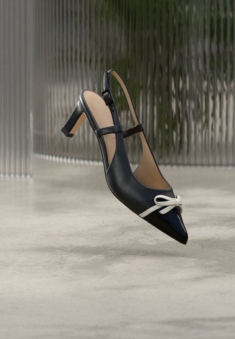 Μαύρο ψηλοτάκουνο παπούτσι με λουράκι και μυτερή μύτη, διακοσμημένο με λευκή λεπτομέρεια φιόγκου, τοποθετημένο σε φόντο με υφή γκρι αποχρώσεων.