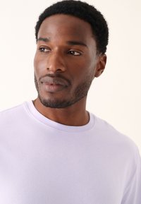 Lilanvärinen lyhythihainen t-paita pyöreällä pääntiellä. Sileä kangas, kaulanauhassa näkyy vain vähän saumoja. Yksinkertainen, yksivärinen malli.