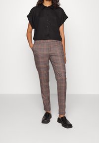 Czarna krótko rękawowa koszula zapinana na guziki w połączeniu z szarymi spodniami w kratę z czerwonymi akcentami, zestawiona z czarnymi butami wsuwanymi.