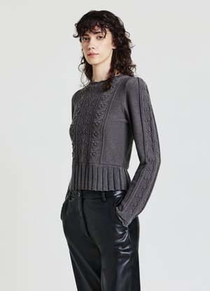 Grauer Strickpullover mit strukturiertem Muster, geripptem Saum und langen Ärmeln, kombiniert mit schwarzen Lederhosen.