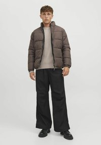 Giubbotto blu chiaro con collo alto, design trapuntato, zip nera e polsini elasticizzati, abbinato a pantaloni neri a gamba larga e scarpe nere.