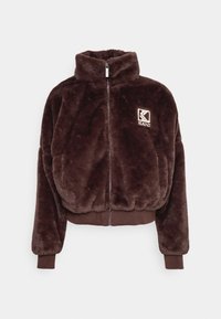 Brązowa kurtka na zamek z sztucznego futra z wysokim kołnierzem, elastycznymi mankietami i dołem. Na lewej piersi naszyte logo w tonacji kolorystycznej. Miękka tekstura.