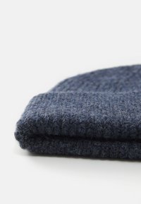 Berretto di lana a coste blu scuro, piegato piatto su una superficie bianca, evidenziando la texture e le fibre morbide.