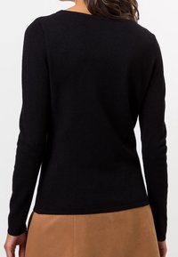 Zwarte lange mouwen top van textuurstof, ronde halslijn en getailleerd ontwerp, gecombineerd met een tan rok. Naaddetails aan de zoom.