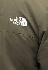 Φυστικί πράσινο μπουφάν με λευκό κεντημένο λογότυπο «The North Face» στην περιοχή του πάνω μέρους του στήθους.