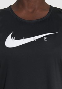 Camiseta deportiva negra hecha de una tela suave, con un logo de Nike en blanco prominente y letras en el pecho, con un cuello redondo.