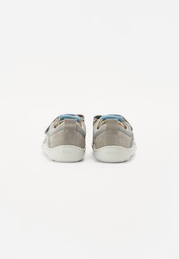Grå semsket og mesh sneakers med blå detaljer, med en teksturert overflate og en hvit gummisåle. Bakfra vises justerbar stropp.
