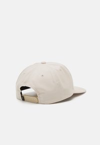 Beige cap med en buet skygge, fremstillet af bomuld. Har en struktureret overflade, ventilationshuller og en justerbar plastikrem bagpå.