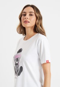 Witte t-shirt met korte mouwen met een grafische print van een panda met een roze hoed en tekst. Opvallende rode accenten op de mouw. Soepele stoftextuur.