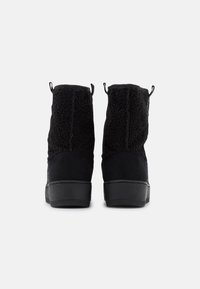 Stivali alla caviglia neri con un materiale superiore morbido al tatto, accentuati da una base nera liscia e una suola testurizzata. Presentano delle linguette per facilitarne l'indossamento.