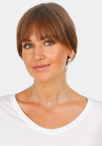 Silver layered choker necklace featuring three strands and a small circular pendant, worn over a white shirt with a wide neckline.